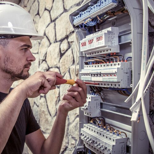 a male electrician works in a switchboard with an electrical con